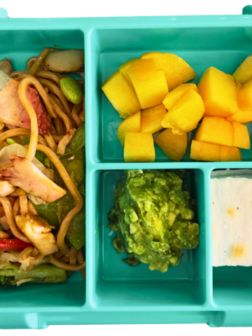 A bento box lunch with yakisoba, peach, avocado and crackers.