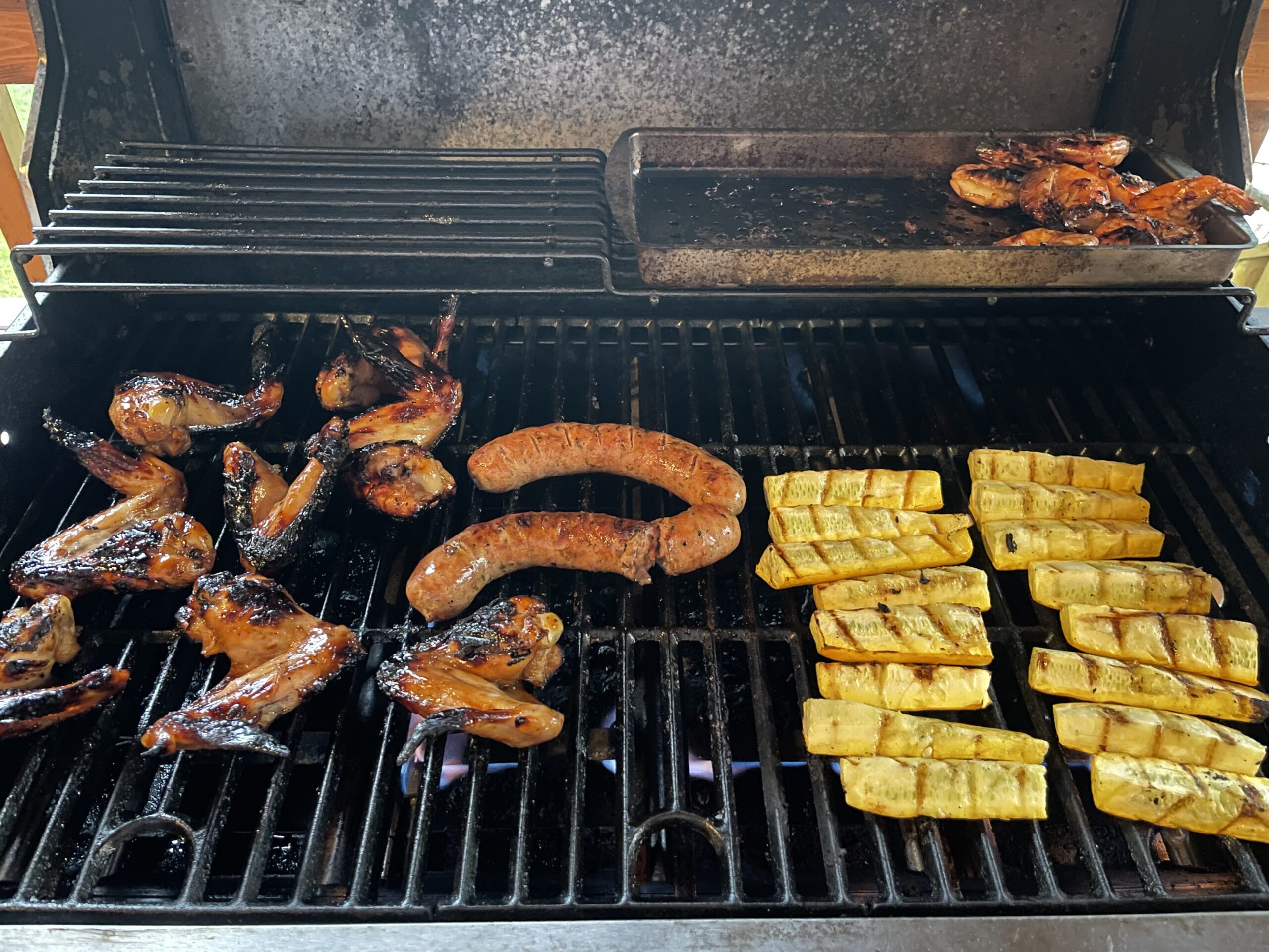 Grilled chicken wings, sausages, shrimps and zucchini on bbq.